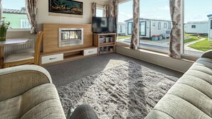 A living room with a fireplace, television, and large windows overlooking a residential area. - 3 bedroom accommodation in California Cliffs (California Cliffs)