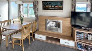 A cozy living room with a fireplace, a dining area with wooden furniture, a television, and a bookshelf. - 3 bedroom accommodation in California Cliffs (California Cliffs)