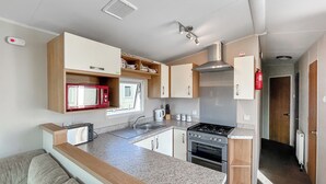 A compact kitchen with a microwave, stove, sink, and wooden cabinets. - 3 bedroom accommodation in California Cliffs (California Cliffs)