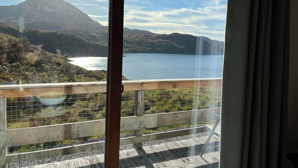 Une vue depuis une fenêtre donnant sur un lac, avec des montagnes en arrière-plan.