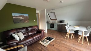 Un salon moderne avec un canapé en cuir, une table à manger avec des chaises, un coin cuisine équipé d’un micro-ondes et d’un four, et un mur d’accent de couleur verte.