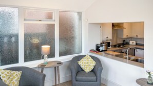 A modern kitchen with a stove, microwave, and sink. There are two grey armchairs with patterned cushions. A small table with a lamp is near the window. - 2 bedroom accommodation in Crook, near Bishop Auckland (Crook, near Bishop Auckland)