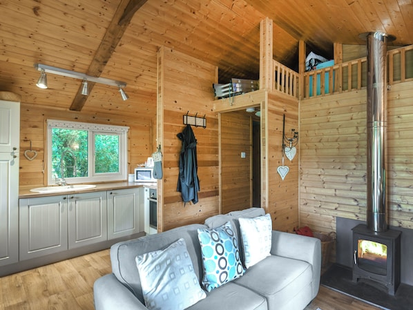 A wooden cabin interior with a sofa, a kitchenette, a stove, and a loft bedroom.
