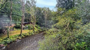 Una baita sul fiume con veranda e posti a sedere all'aperto, circondata da un fitto bosco.