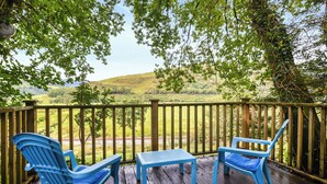 Un terrazzo in legno con sedie blu e un tavolo, affacciato su un paesaggio erboso.