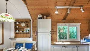 Una cucina con mobili in legno, un lavandino bianco, una finestra con vista su vegetazione, un lampadario e uno scaffale con utensili da cucina.