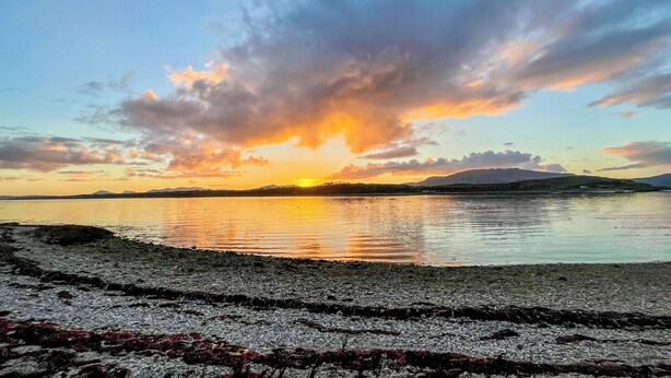 A sunset over a calm lake with a rocky shoreline.