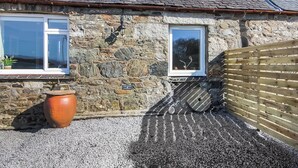 A stone building with a sloped roof, two windows, a gravel driveway, and a wooden fence.