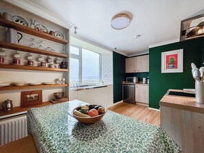 A kitchen with wooden shelves, a bowl of fruit, a window, and a green wall.