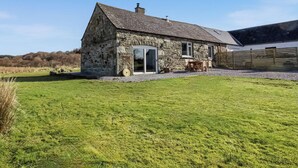 A stone farmhouse with a sloped roof, a large open door, and a fenced yard.