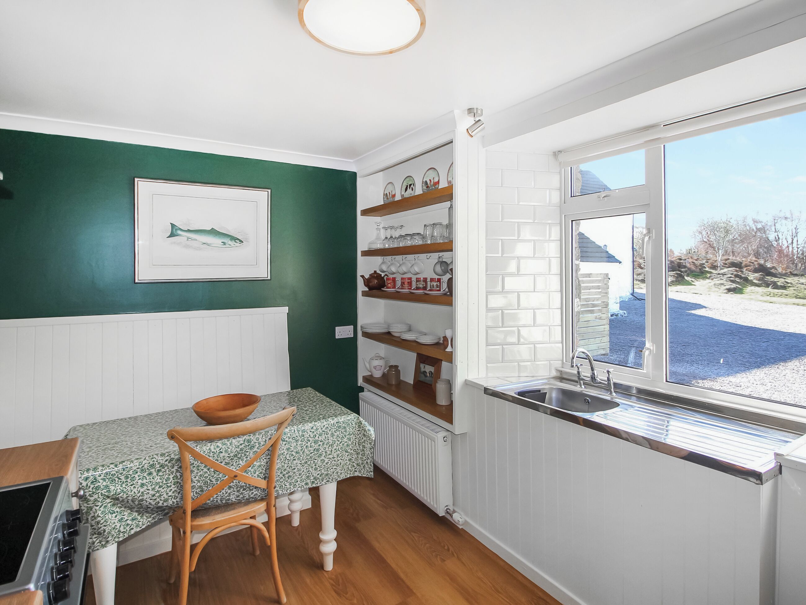 A kitchen with a dining table, chairs, a window, and a shelf with dishes and glasses.