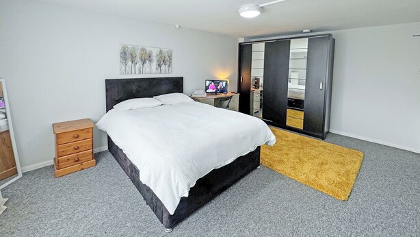 A bedroom with a bed, a desk, a wardrobe, and a mirror.