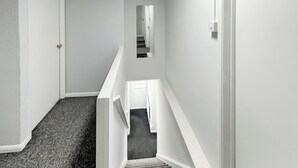 A staircase with carpeted steps leading to a landing, white walls, and a door at the top.