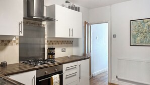 A modern kitchen with white cabinets, a stainless steel range hood, and a gas stove. - 2 bedroom accommodation in Arlecdon (Frizington)