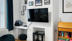A living room with a TV mounted on the wall, a bookshelf with board games, and framed pictures on the wall. - 2 bedroom accommodation in Arlecdon (Frizington)