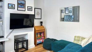 A living room with a flat-screen TV, a bookshelf, a sofa, and a mirror on the wall. - 2 bedroom accommodation in Arlecdon (Frizington)