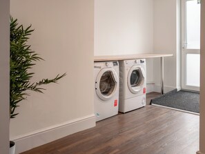 A laundry room with two front-loading washing machines, a wooden floor, and a door leading outside.