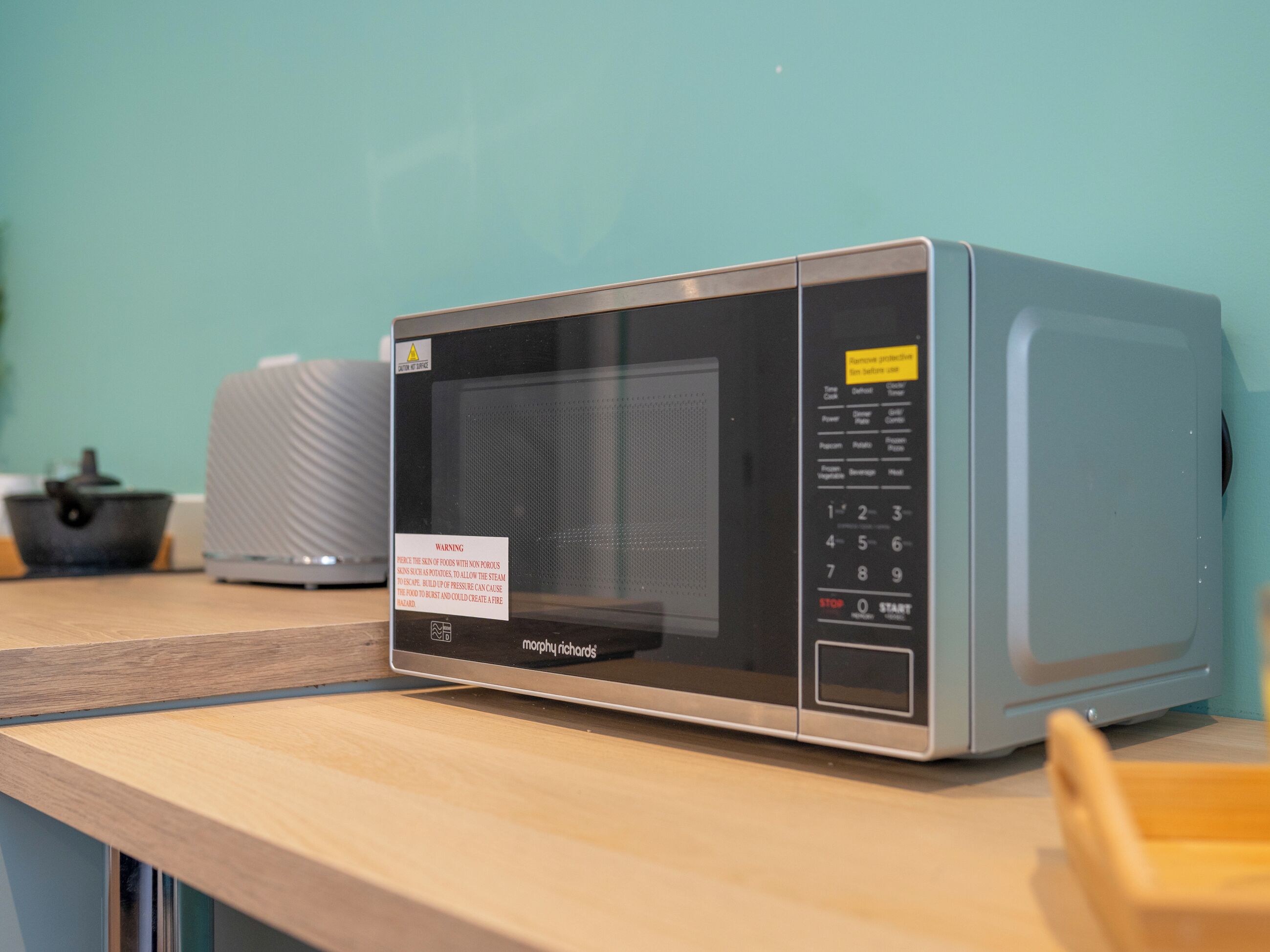 A microwave oven on a wooden countertop with a warning label, a control panel, and a small tray.