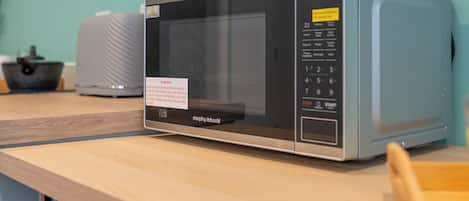 A microwave oven on a wooden countertop with a warning label, a control panel, and a small tray.