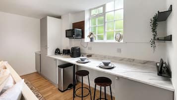 Une cuisine moderne avec un plan de travail blanc, deux tabourets de bar, un four à micro-ondes, une machine à café et une fenêtre donnant sur un beau paysage.
