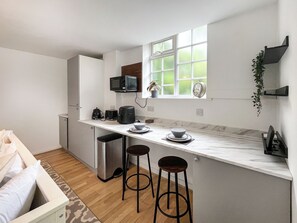 A modern kitchen with a white countertop, two bar stools, a microwave, a coffee maker, and a window with a view.