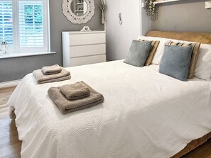 A bedroom with a bed, pillows, a dresser, a mirror, and a window with blinds.