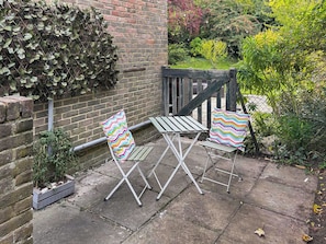 A patio with two folding chairs and a table, surrounded by a brick wall and greenery. - A lovely cosy property in a lovely location with stunning scenery. (Kenley, near Surrey)