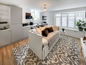 A compact living space with a kitchenette, a sofa, a patterned rug, and a window with blinds.