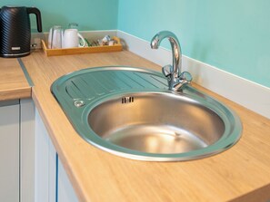A kitchen sink with a modern faucet, a kettle, and a tray with cups and a jar. - Hilltop Apartment 1 - UK50591 (Earl Shilton)