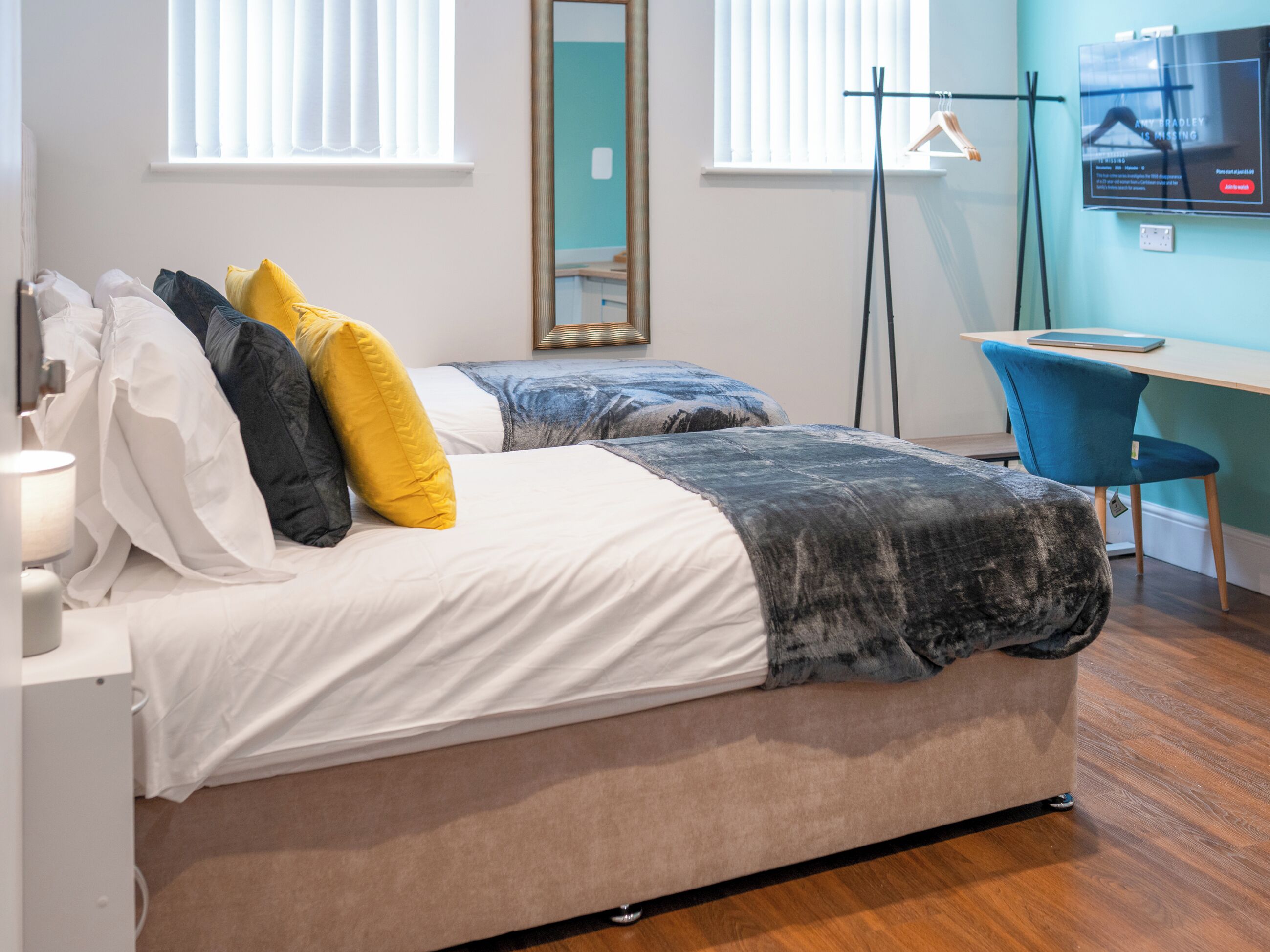 A hotel room with two beds, a desk, a chair, and a TV on the wall.
