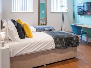 Habitación de hotel con dos camas, un escritorio, una silla y un televisor en la pared.