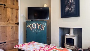 A cozy room with a wooden door, a TV on a cabinet labeled "TOYS," a fireplace, and a framed artwork on the wall. - 3 bedroom accommodation in Ampleforth, near Helmsley (Ampleforth, near Helmsley)