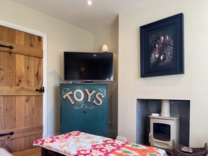 A cozy room with a wooden door, a TV on a cabinet labeled "TOYS," a fireplace, and a framed artwork on the wall.