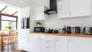 Une cuisine moderne avec des armoires blanches, un plan de travail en bois, un micro-ondes noir, une bouilloire et une machine à café. Une fenêtre offre une vue sur l’extérieur.