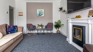 Un salon comprenant un canapé, deux fauteuils, une cheminée, un téléviseur et une étagère fixée au mur.