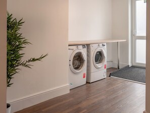 A laundry room with two front-loading washing machines, a wooden bench, a potted plant, and a door.