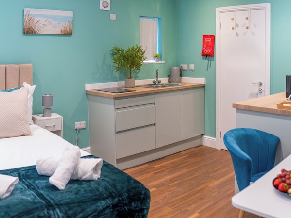 A room with a bed, a desk, a chair, a sink, and a plant.