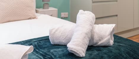 Una cama bien hecha con sábanas blancas y una manta color turquesa.