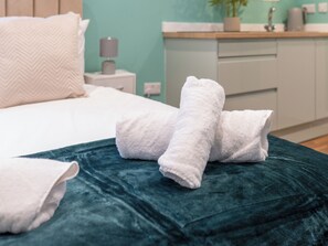A neatly made bed with white linens and a teal throw blanket.