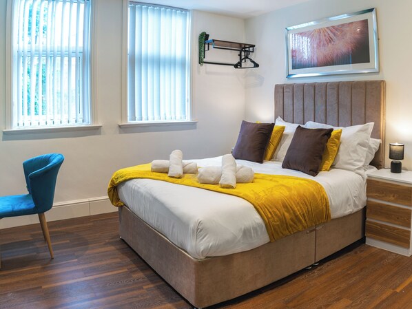 A modern hotel room with a large bed, a bedside table, a chair, and a window with blinds.