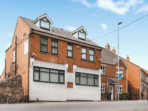 A two-story brick building with multiple windows and a sign for Hilltop Serviced Apartments.