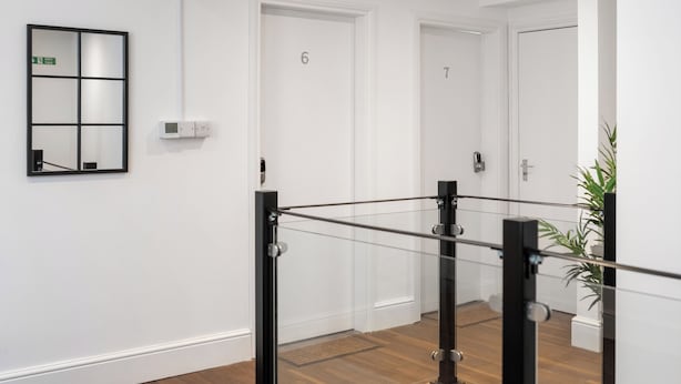 A modern hallway with a glass railing, white doors numbered 6 and 7, and a green emergency exit sign. - Hilltop Apartment 7 - UK50599 (Earl Shilton)