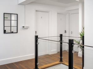 A modern hallway with a glass railing, white doors numbered 6 and 7, and a green emergency exit sign.