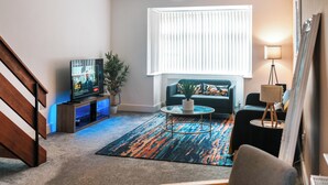 Un salon avec un canapé, une table basse, un téléviseur et un escalier.