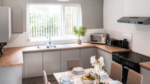 Une cuisine moderne équipée d’un four à micro-ondes, d’un grille-pain et d’une cuisinière intégrés. On y trouve une table à manger, mise avec des assiettes et un saladier rempli de fruits.