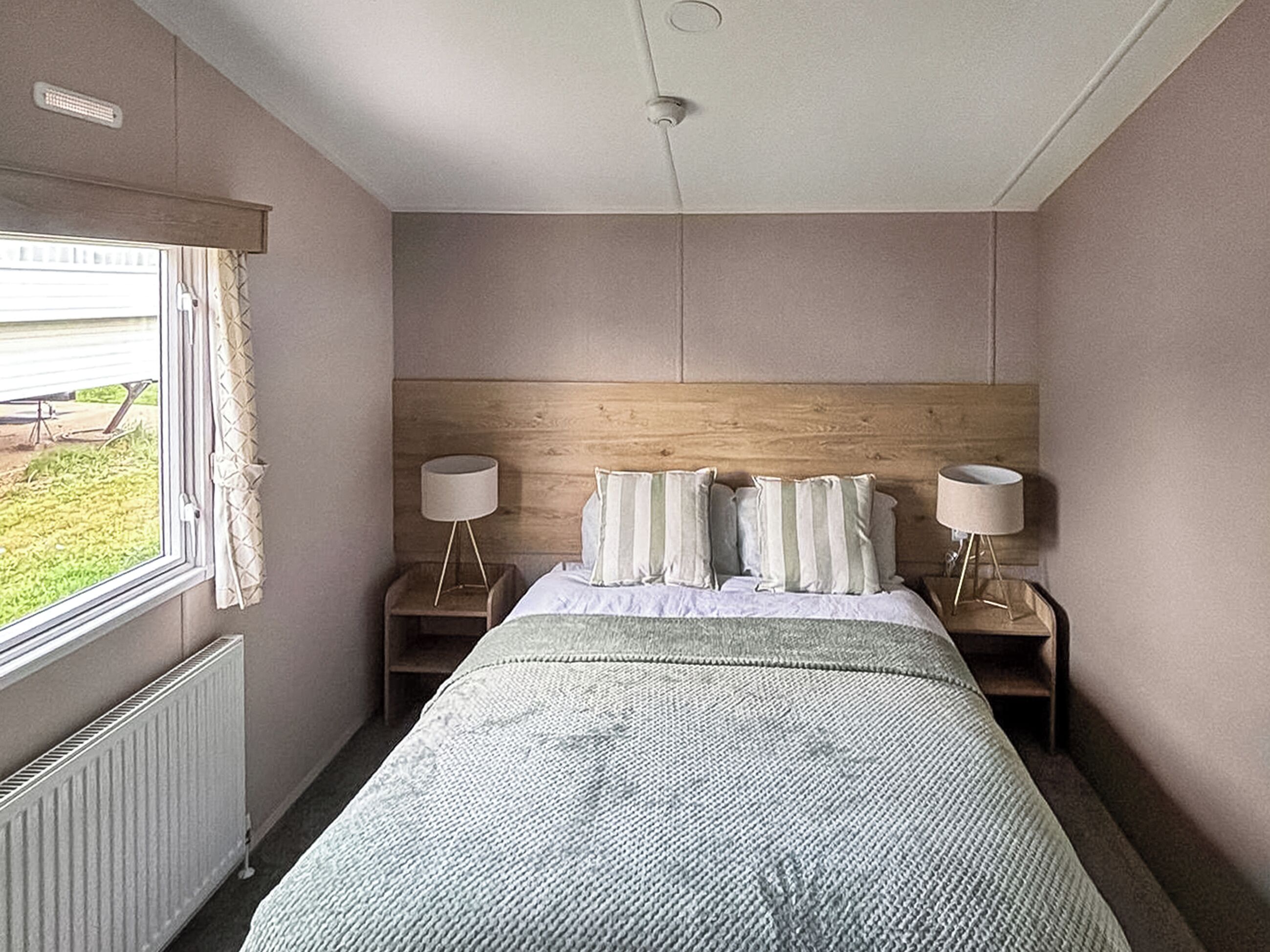 Ein Hotelzimmer mit einem Bett, zwei Nachttischen, einem Fenster mit Vorhängen und Blick ins Freie.