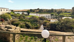 Vista a la orilla del río con un puente de madera, muros de piedra y un farol.