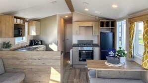 Cocina compacta con estufa, horno, microondas y refrigerador. Hay una zona de comedor con mesa y bancos.