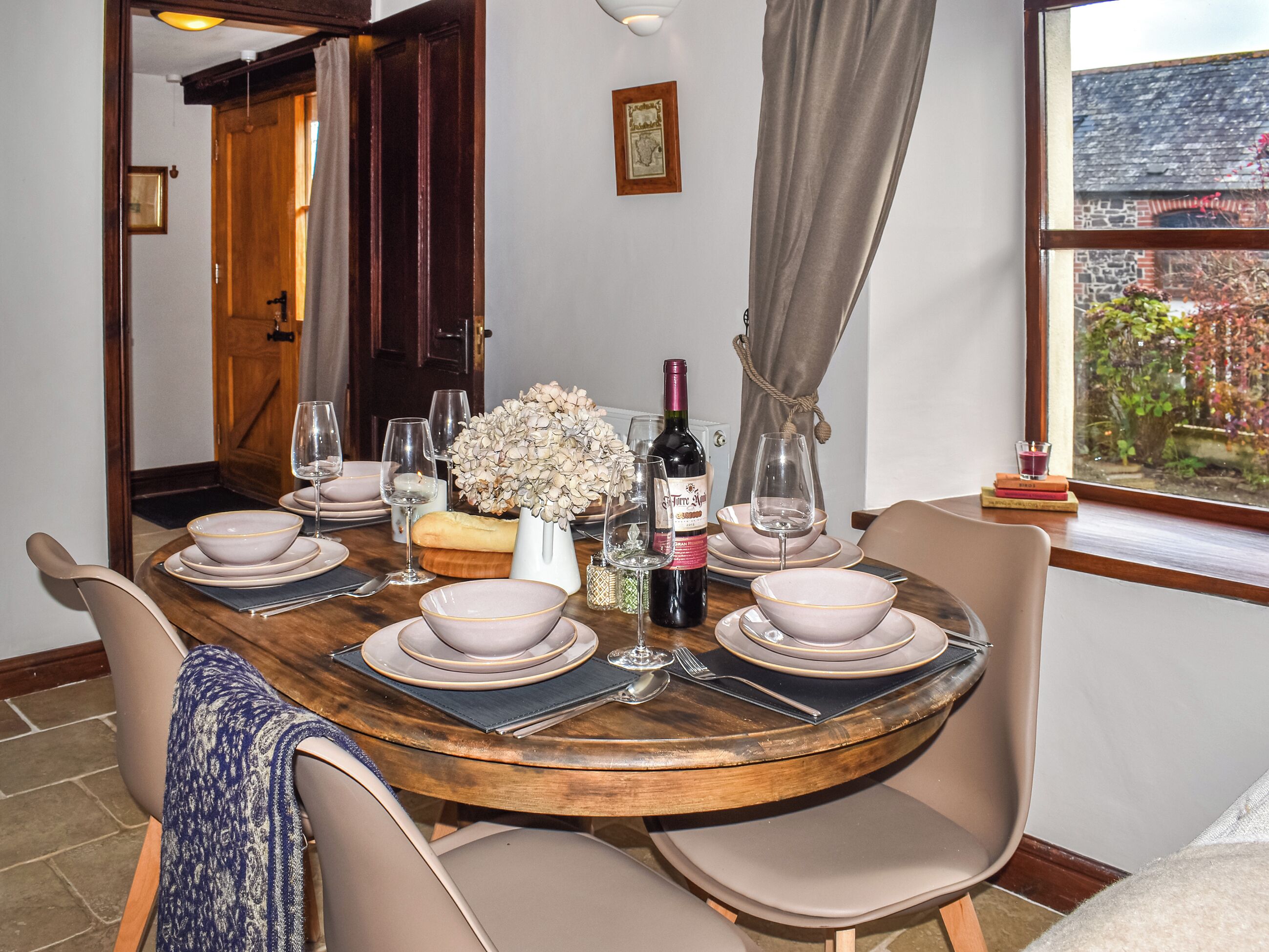 A dining table set with plates, glasses, a bottle, and a vase.