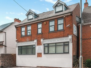 A two-story serviced apartment building with a brick facade, multiple windows, and a sign indicating the address and contact information.